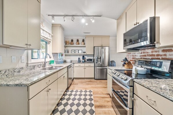A modern kitchen with granite countertops, stainless steel appliances, and a checkered floor rug.
