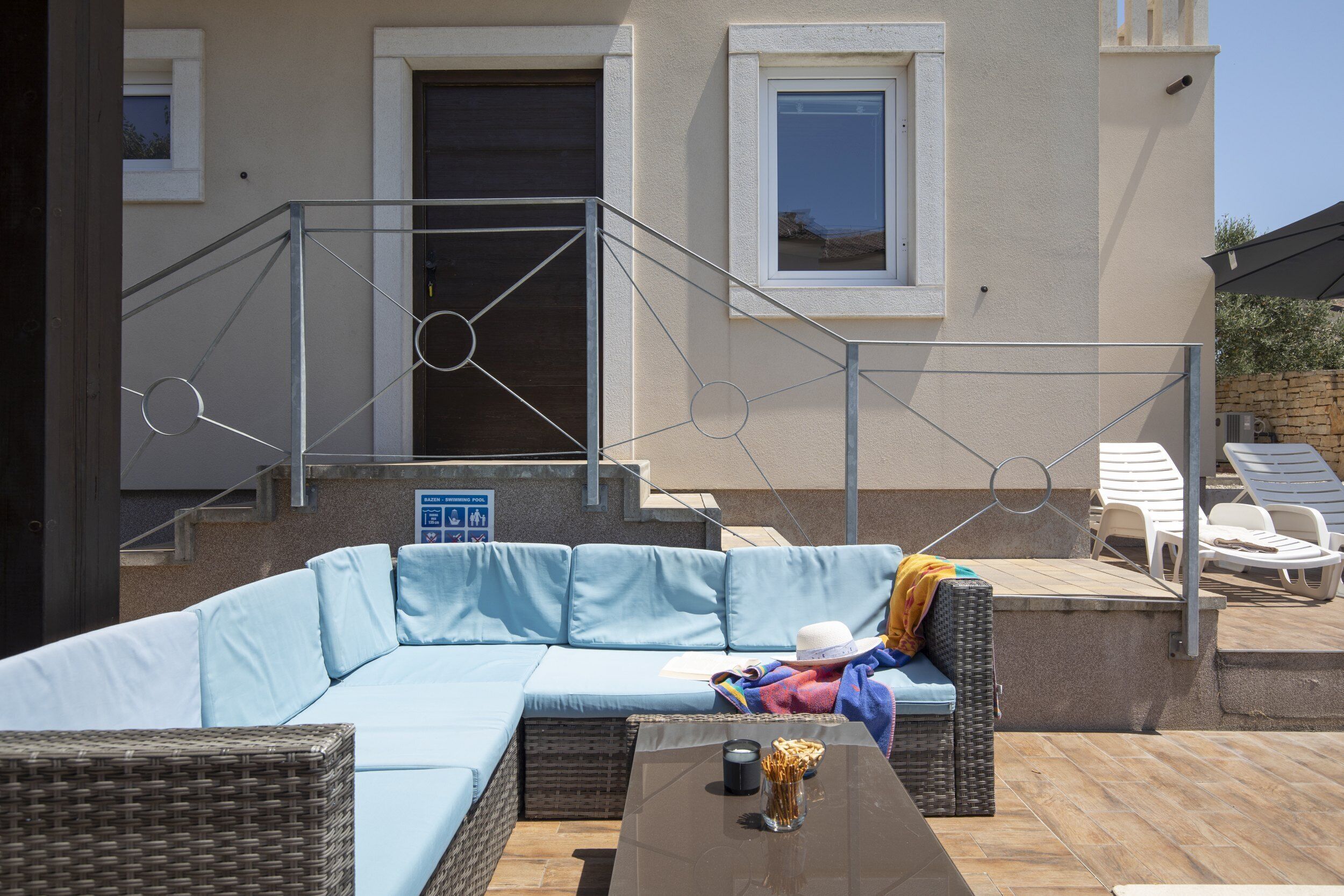 A sunlit outdoor seating area with a light blue sofa, wicker furniture, and a glass table.