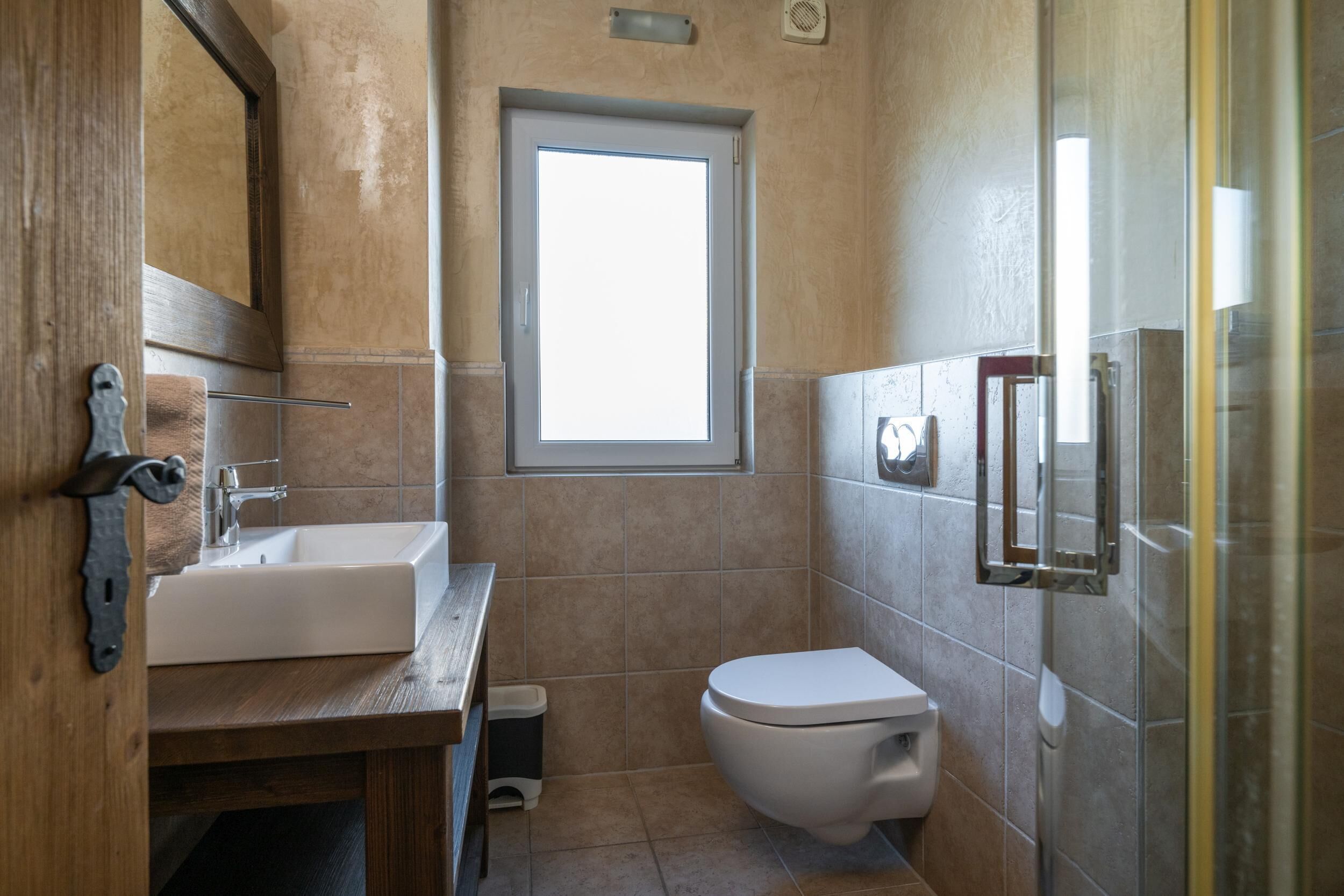 Een badkamer met een houten wastafel, een witte wasbak, een toilet en een raam.