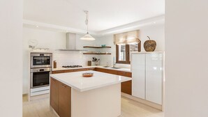 A modern kitchen with white cabinetry, a central island, built-in oven, and a hanging light fixture.
