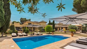 A swimming pool with lounge chairs and umbrellas, surrounded by a landscaped garden and buildings.