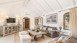 A spacious living room with a wooden coffee table, a sofa, and a television. There is a cabinet with glass doors and a wooden door leading to another room.