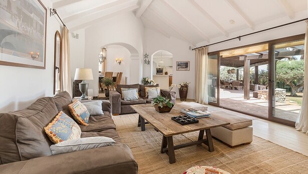 A spacious living room with a large sofa, a wooden coffee table, and a view of the outdoor patio through large sliding glass doors.