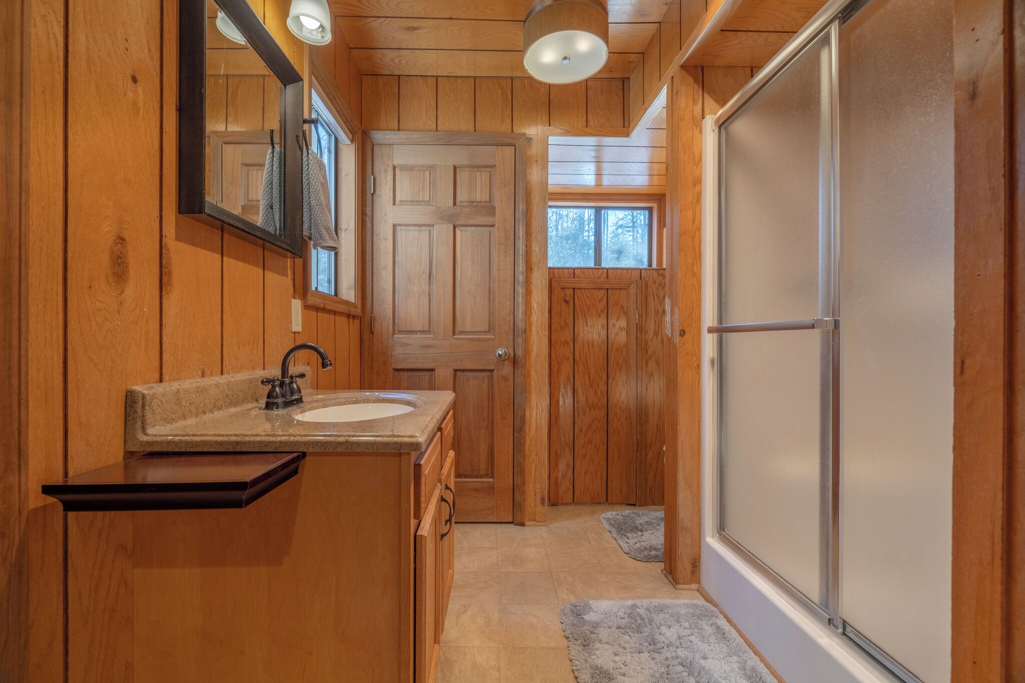 Une salle de bain rustique, aménagée dans une cabane en bois, avec un lavabo, un miroir et une douche.