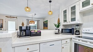 Cocina moderna con muebles blancos, una barra de café, microondas, licuadora y lámparas colgantes.