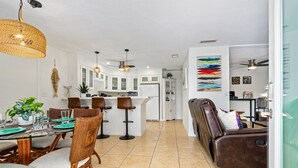 Amplia sala de estar con una mesa de comedor preparada para cuatro personas, un sofá de cuero marrón y una cocina al fondo.