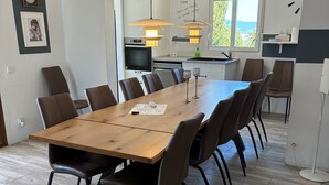 A dining area with a long wooden table and brown chairs, a kitchen in the background, and a clock on the wall. - Villa with heated pool and private padel court (Pinos de Alhaurín)