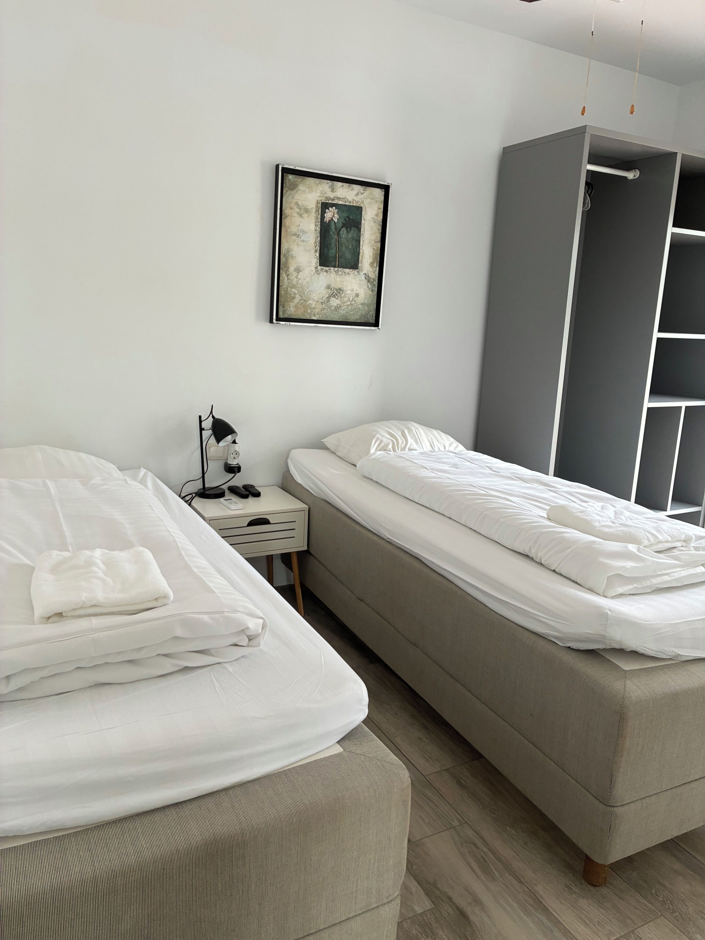 Habitación de hotel con dos camas, una mesita de noche con lámpara, un cuadro en la pared y un armario.