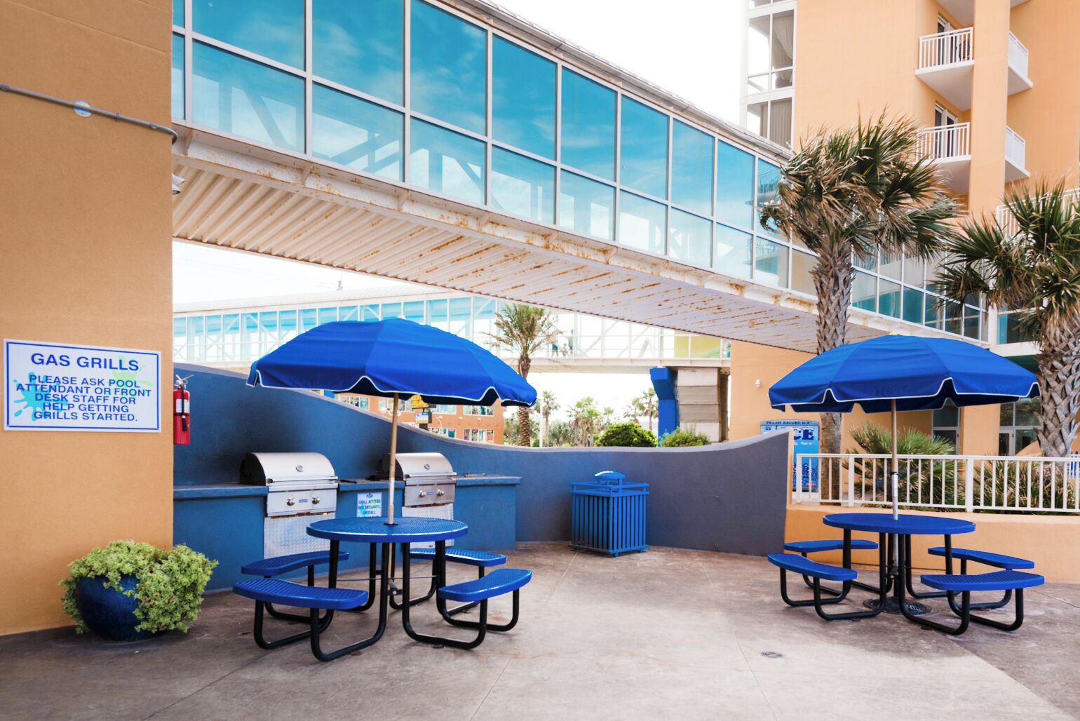 Un patio al aire libre con parrillas a gas, sombrillas azules y asientos.