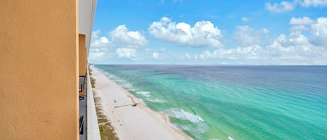 A beach view from a balcony with clear turquoise water and a sandy shore.