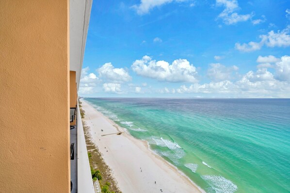 A beach view from a balcony with clear turquoise water and a sandy shore.