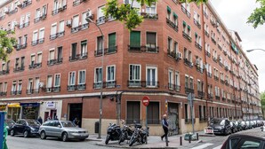 A multi-story red brick building with balconies, a 'SARA' sign, parked cars, and motorcycles on the street. - Cozy apartment close to Atocha and Retiro, Madrid - Cuore Apartments (Madrid)