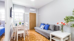 A modern living room with a dining area, a grey sofa with blue and white cushions, a white coffee table, and a wooden herringboard floor. - Cozy apartment close to Atocha and Retiro, Madrid - Cuore Apartments (Madrid)