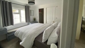 A bedroom with a bed, a window, a door, and a small table. - Paddock View - Snetterton, Norfolk (Norwich)
