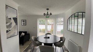 A modern dining area with a round table, four chairs, a chandelier, and large windows. - Paddock View - Snetterton, Norfolk (Norwich)