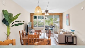 Un comedor con una mesa y sillas de madera, una lámpara colgante y vistas al exterior a través de amplios ventanales.