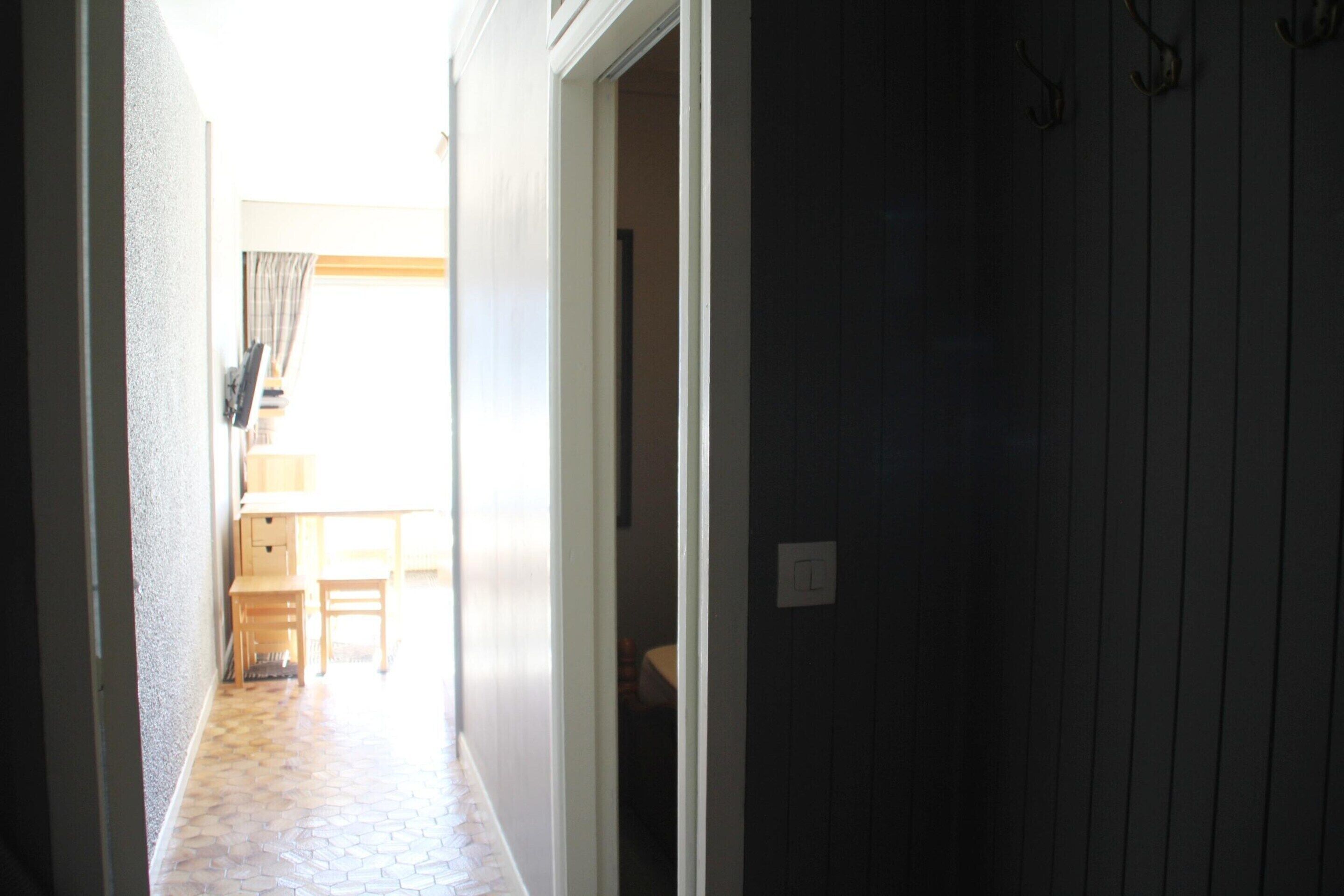 A narrow hallway with a tiled floor leading to a room with a bed and a window.