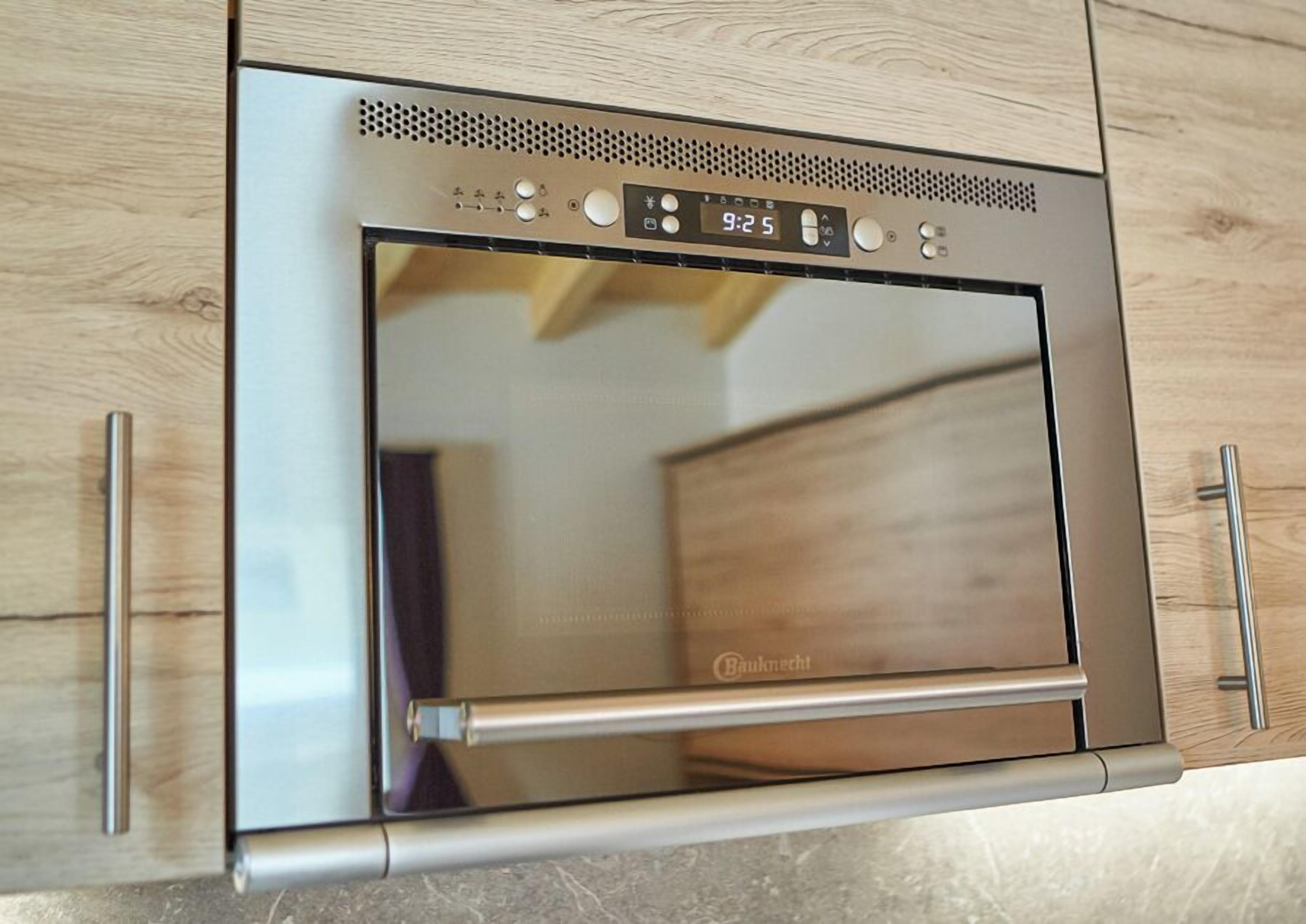 A stainless steel oven with a digital clock displaying 9:25, built into a wooden cabinet with a handle.