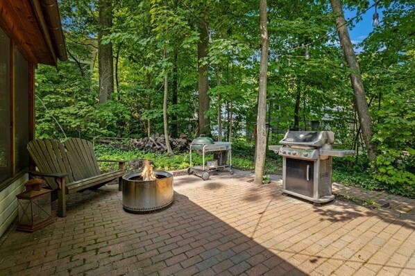 An outdoor patio with a fire pit, a grill, and a wooden chair. - Lakeside Home With 40 FT of Private Beach! (Lakeside)