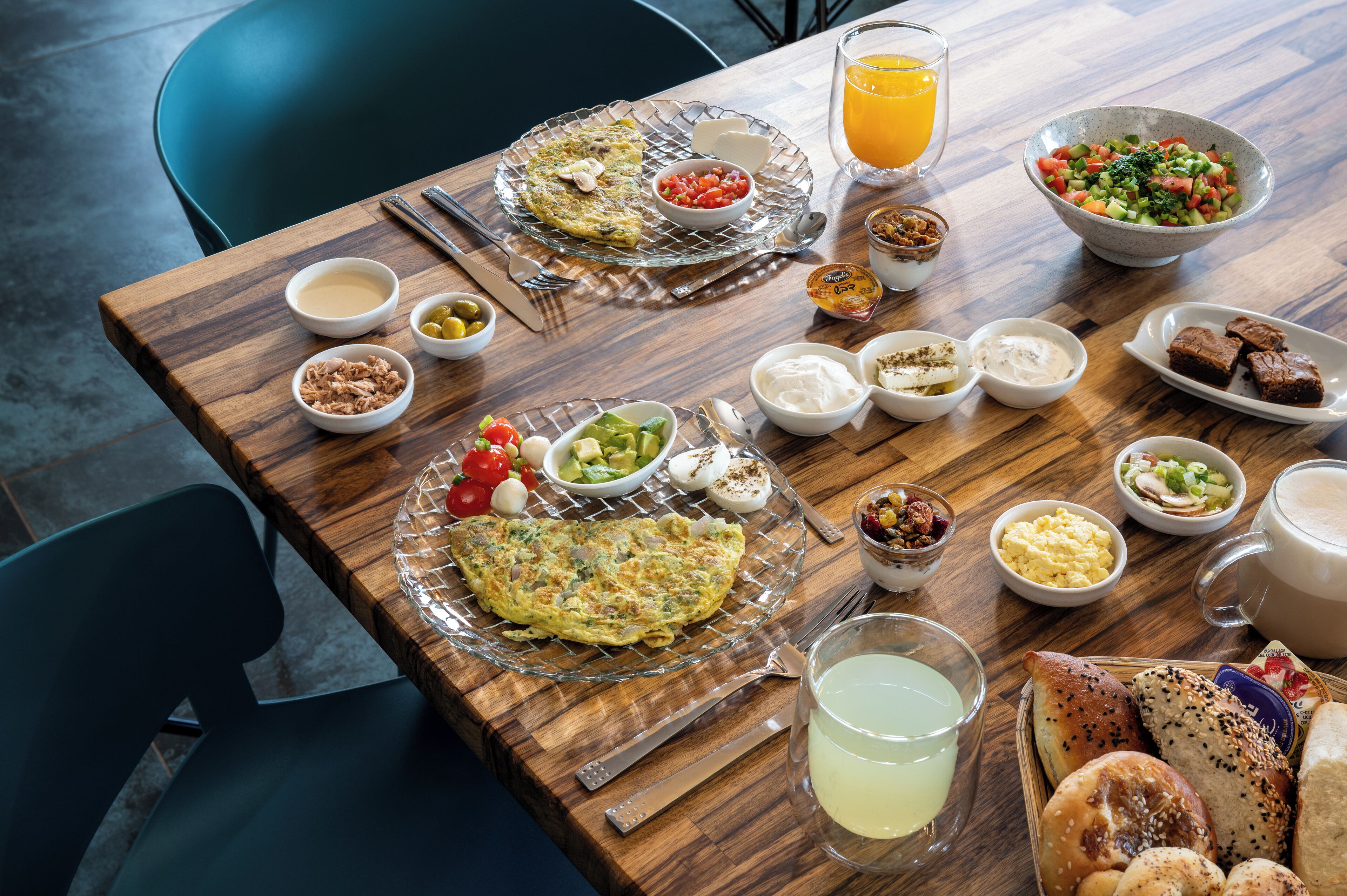 Uma mesa de café da manhã com diversos pratos, incluindo um omelete, uma tigela de frutas e um copo de suco de laranja.