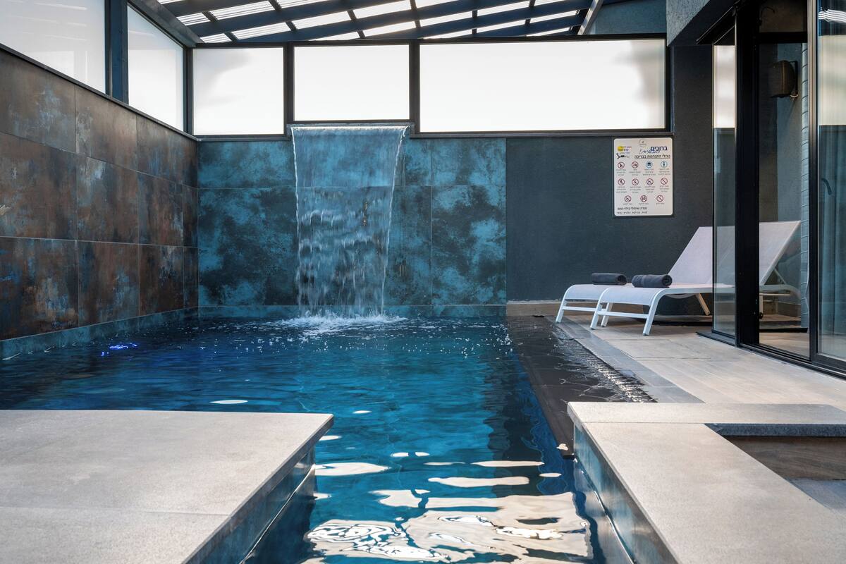 Une piscine intérieure agrémentée d’une cascade, de chaises longues et d’un mur en verre.