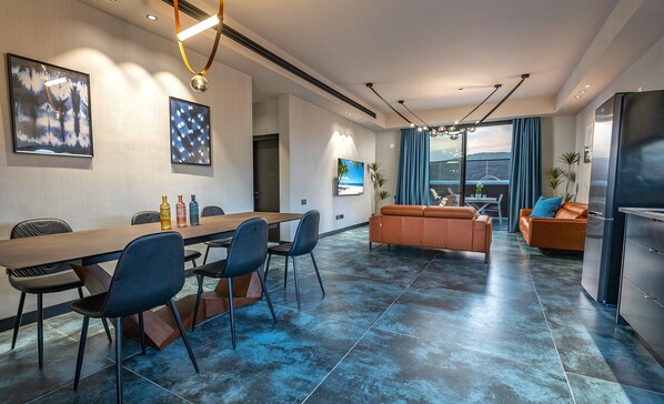 Un salon moderne avec un coin repas, comprenant une grande table, des chaises, un canapé et un téléviseur.