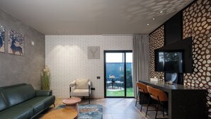 Een moderne woonkamer met een bank, salontafel en stoelen, een keuken met een bar, en een grote televisie.