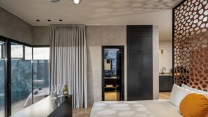 Een moderne hotelkamer met een groot bed, een glazen balkon en een minibar, met uitzicht op het landschap.