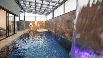 An indoor swimming pool with a glass ceiling, a brick wall, and a white robe hanging on the wall.