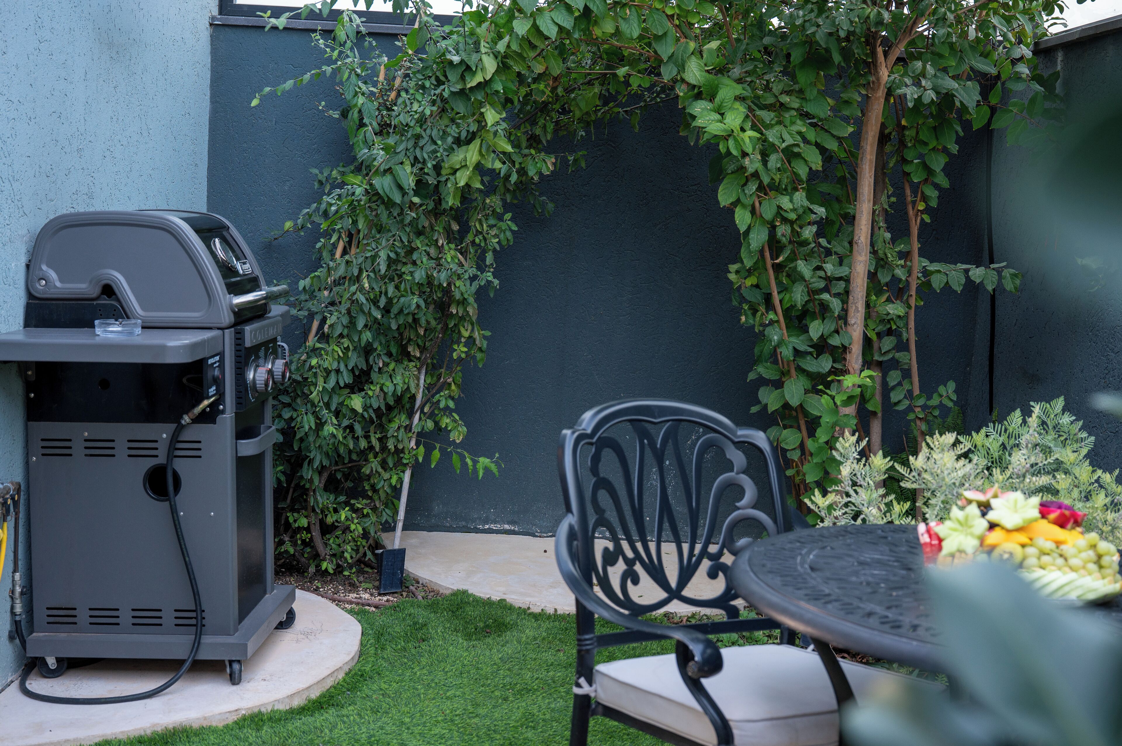 A patio with a grill, a table with fruit, and a chair.