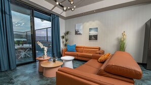Een moderne woonkamer met een grote oranje bank, een witte salontafel en een glazen deur naar een buitenruimte.