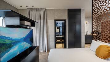 A modern hotel room with a large bed, a flat-screen TV, a wardrobe, a bathroom, and a decorative partition.