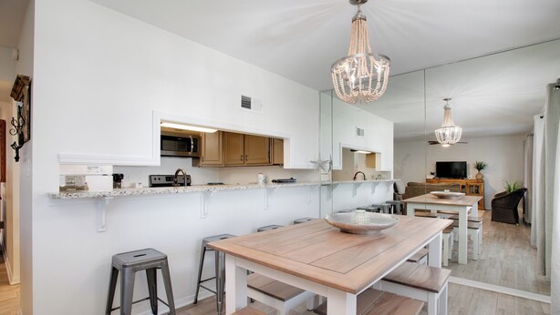 Een moderne keuken met witte kasten, een houten eettafel en barstoelen.