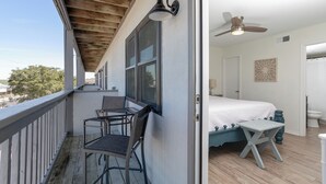 Een balkon met een tafel en stoelen, een plafondventilator, en een slaapkamer met een bed en een klein krukje.