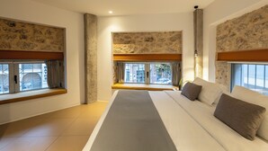 A modern hotel room with a large bed, a window seat, stone wall decor, and a view of the city. - Asomaton by Oniro (Athens)