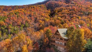 Eine Holzhütte mit Steinunterbau, umgeben von einem Wald im Herbstlaub.
