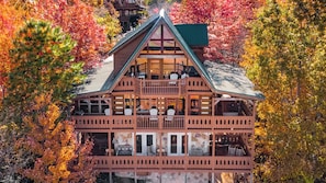 A two-story log cabin with a balcony, surrounded by autumn foliage. - *Spacious 3BD Cabin w/ VIEWS! Hot Tub + Games!* (Sevierville)