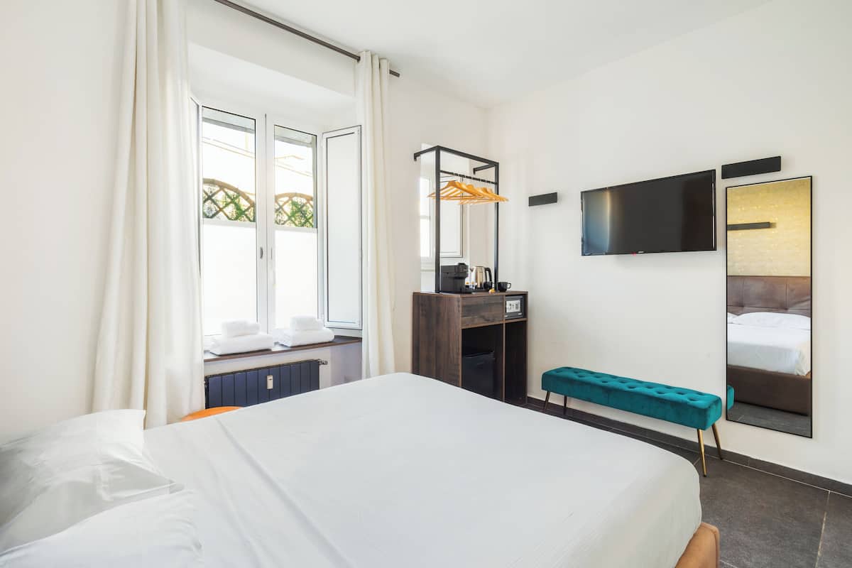 A hotel room with a large bed, a desk with a computer, a TV, and a mirror.