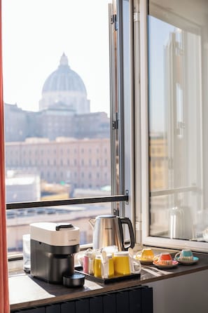 Una finestra con una macchina per il caffè, tazze e un bollitore su un piano di lavoro della cucina. Si intravede una vista di un edificio con una cupola attraverso la finestra.