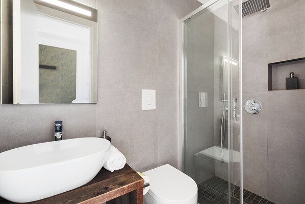 Une salle de bain moderne avec un grand lavabo blanc, un meuble-lavabo en bois, des toilettes et une douche à parois de verre.