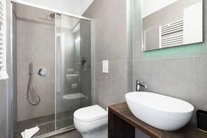 Un bagno moderno con doccia vetro, water bianco e un ampio lavabo su un mobile in legno.