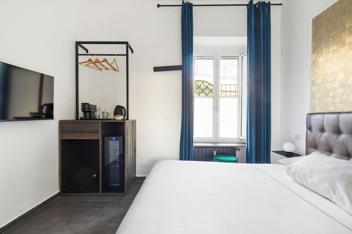 A hotel room with a bed, a desk with a computer, a TV, and a window with curtains.
