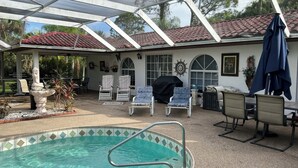 A covered outdoor swimming pool area with lounge chairs, a stone fountain, and a patio with a tiled border.
