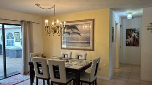 A dining area with a chandelier, a large ocean-themed painting, and a glass table.