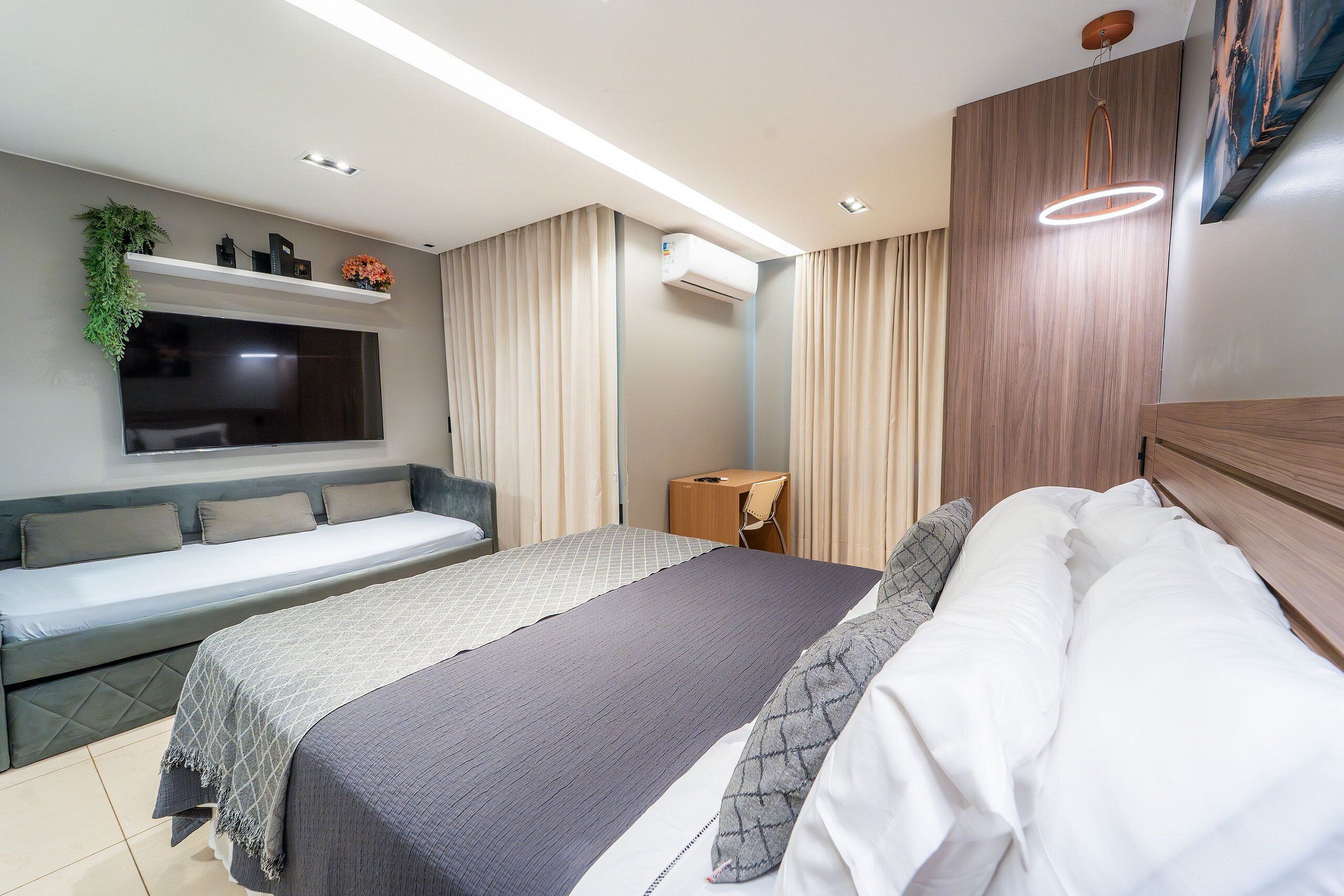 A modern hotel room with a bed, a sofa, a TV, an air conditioning unit, and a desk.