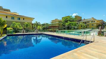 A swimming pool with a wooden deck, surrounded by buildings and greenery.