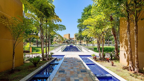 A pool area with a tiled walkway leading to a staircase, surrounded by trees and a building in the background. - The Sun flat (Brasília)