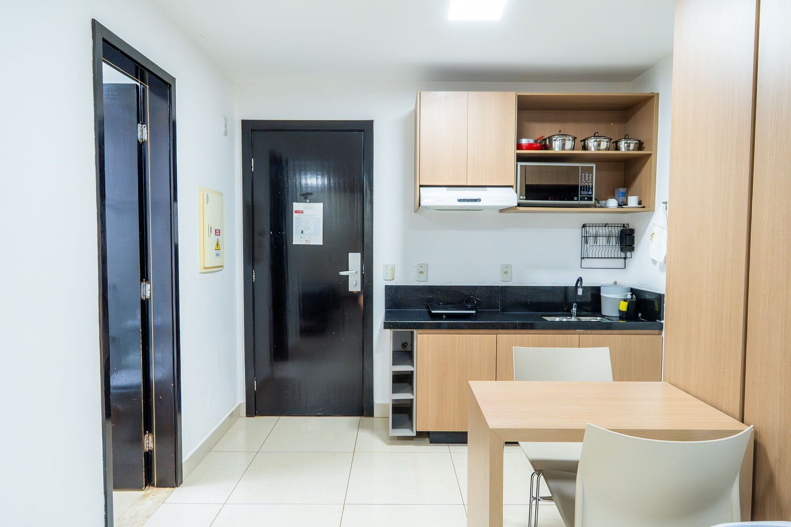 A compact kitchen with a black countertop, wooden cabinets, a microwave, and a sink.