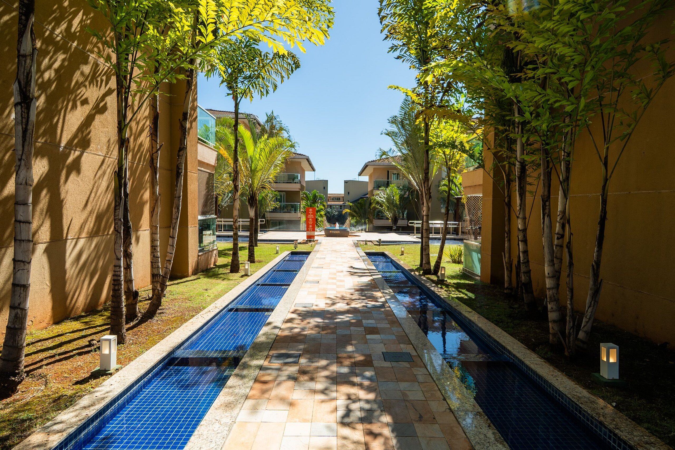 Un espace piscine avec une allée dallée, entouré d’arbres et de bâtiments.