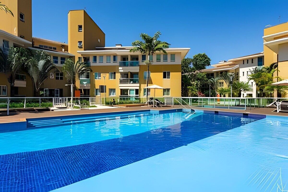Una piscina rodeada de edificios amarillos con balcones, palmeras y zonas de estar al aire libre.